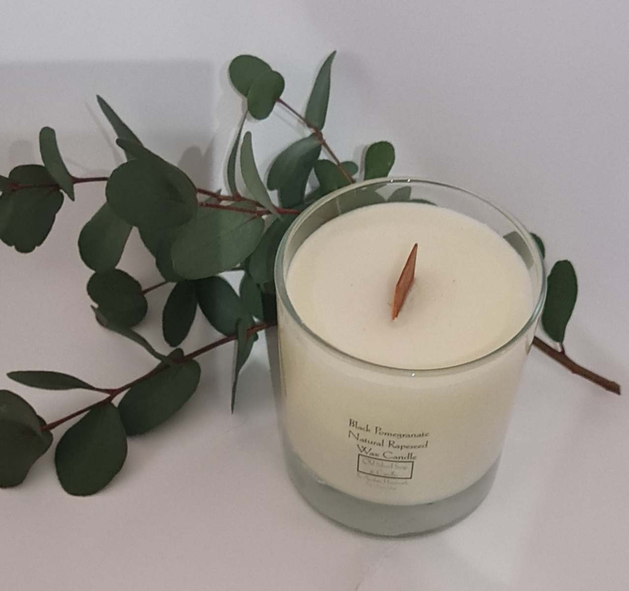 a candle with eucalyptus leaves on a white surface